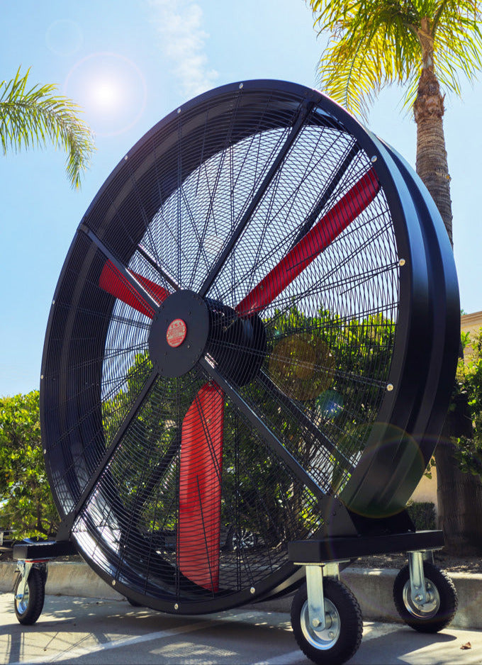 72" Floor Fan with black housing, red blades, metal frame, black and silver casters and metal bearings, product of Industrial Fan Co, with blue sky in the background and palm trees and green bushes