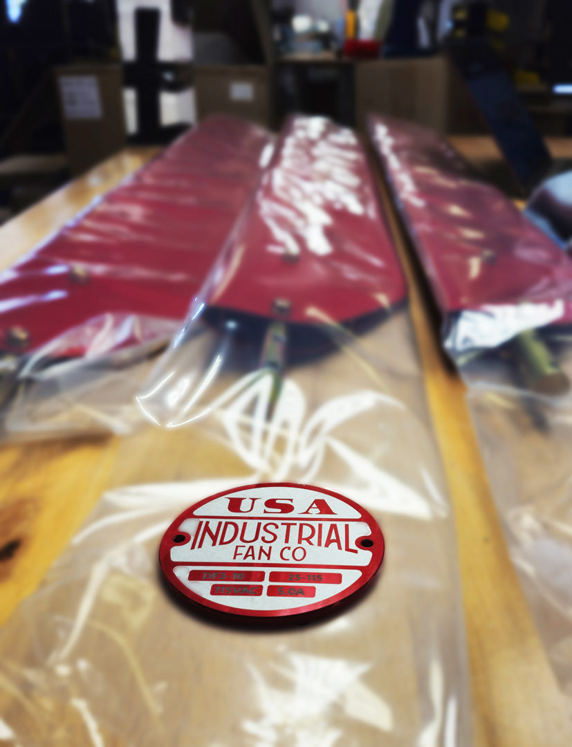 Red and white Industrial Fan Co brand badge logo on a top of red fan blades covered with clear plastic bag with a blurred background.