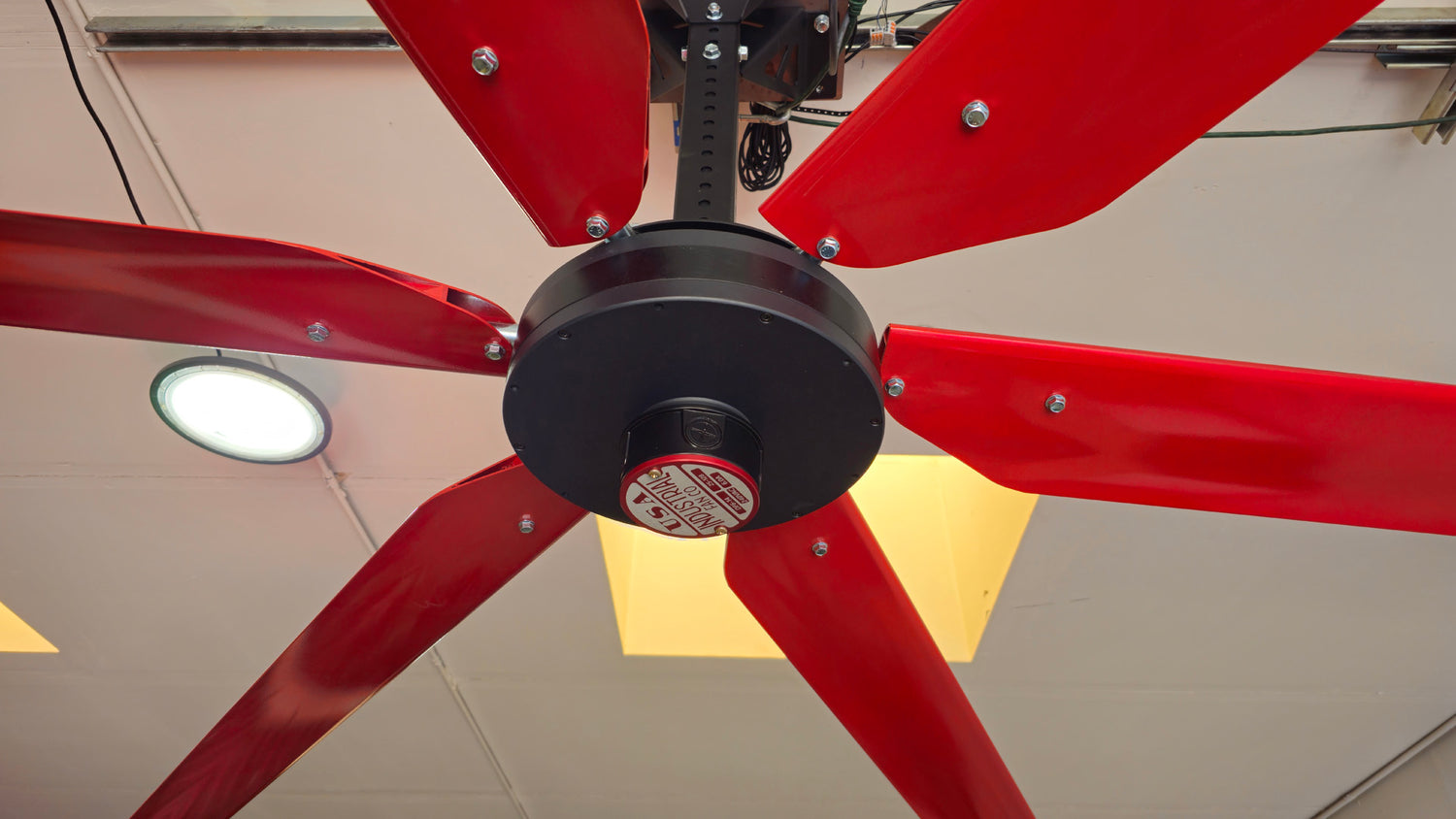 Close up of a wall mount, motor casing, red and silver brand badge and 6 blades for DF6 Red Industrial Ceiling Fan from Industrial Fan Co, mounted on the ceiling