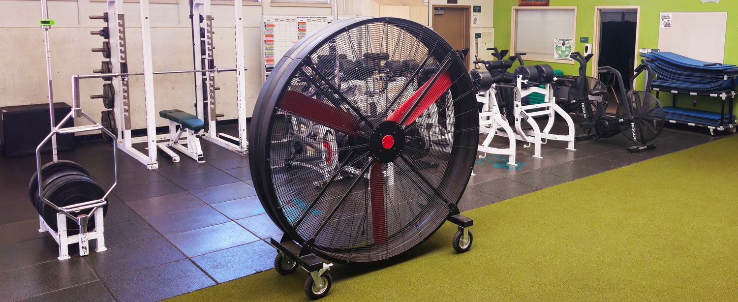 72" Floor Fan with black housing, red blades, metal frame, black and silver casters and metal bearings, product of Industrial Fan Co, in a high-school gym setting with workout equipment in the background