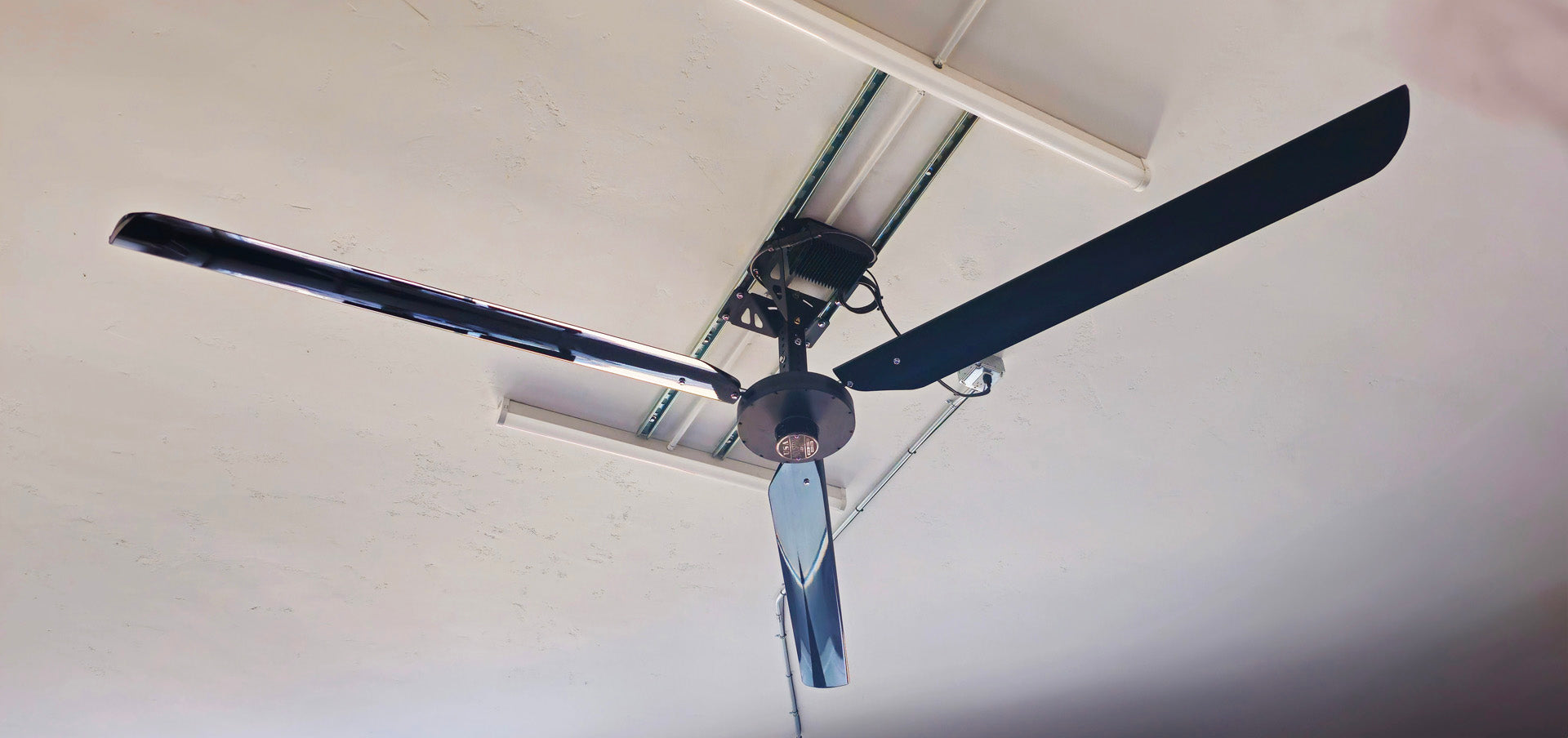 Close up of a telescoping mount, motor, silver brand badge and 6 blades for DF6 Black Industrial Ceiling Fan from Industrial Fan Co, mounted on the ceiling with 2 rectangular lights around it