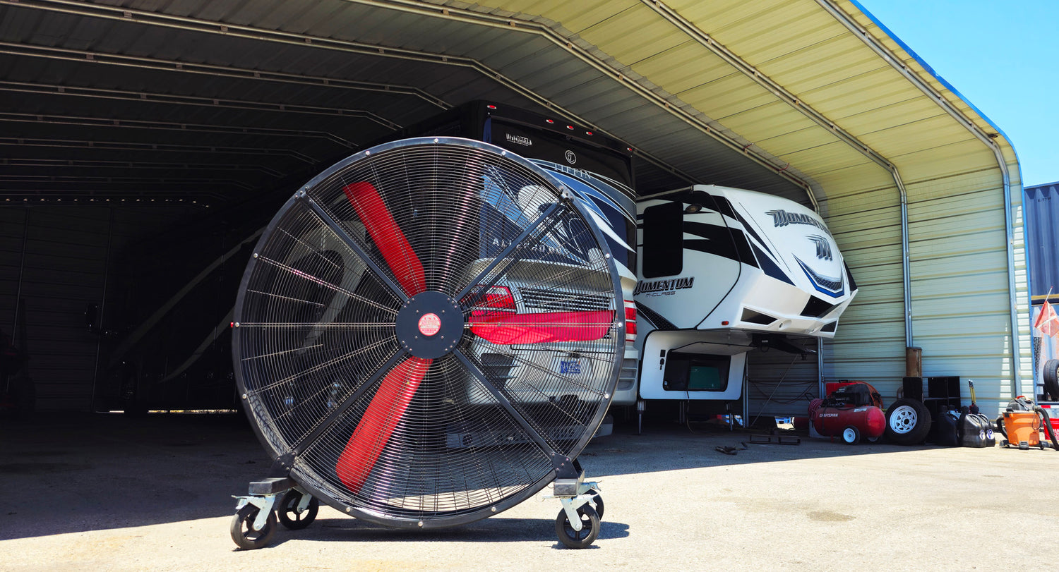72" Floor Fan with black housing, red blades, metal frame, black and silver casters and metal bearings, product of Industrial Fan Co, in front of a hangar garage with a parked house on wheels