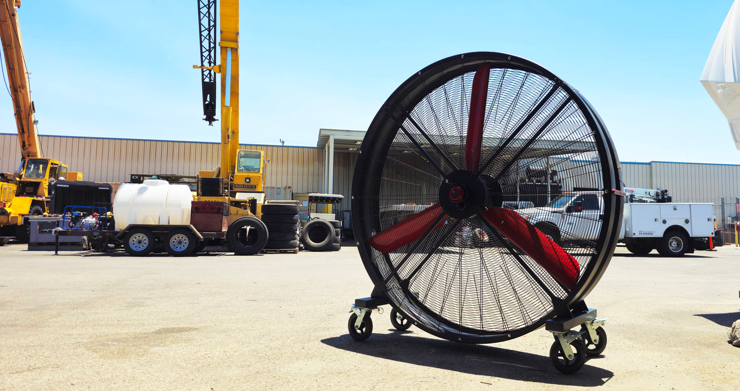 72" Floor Fan with black housing, red blades, metal frame, black and silver casters and metal bearings, product of Industrial Fan Co, in an industrial setup with cranes in the background