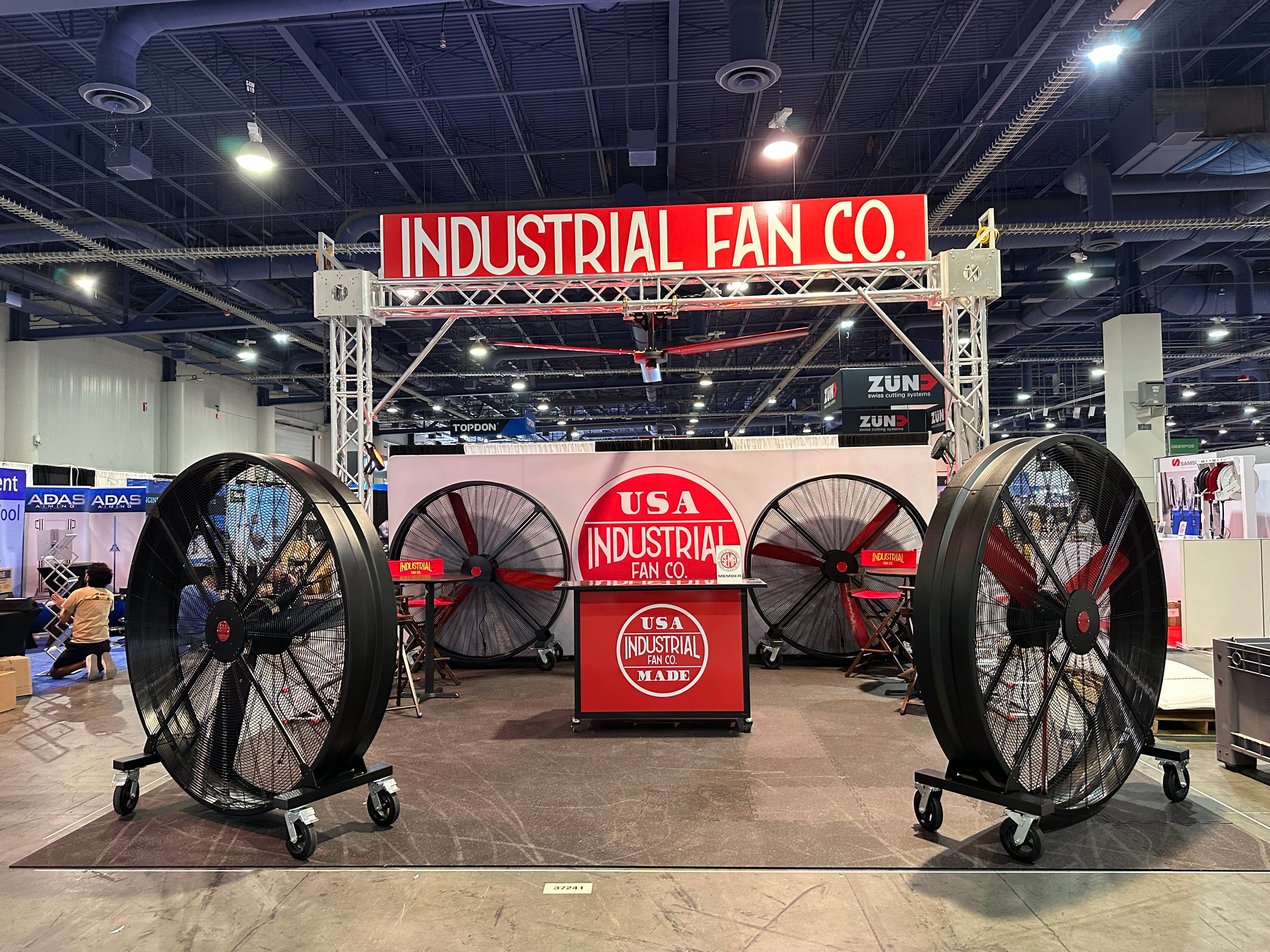 Industrial Fan Co conference booth, with 4 floor fans and one ceiling fan on the metal frame, and square red and black table with huge circular logo of the company, as well as huge logo on a top of the booth