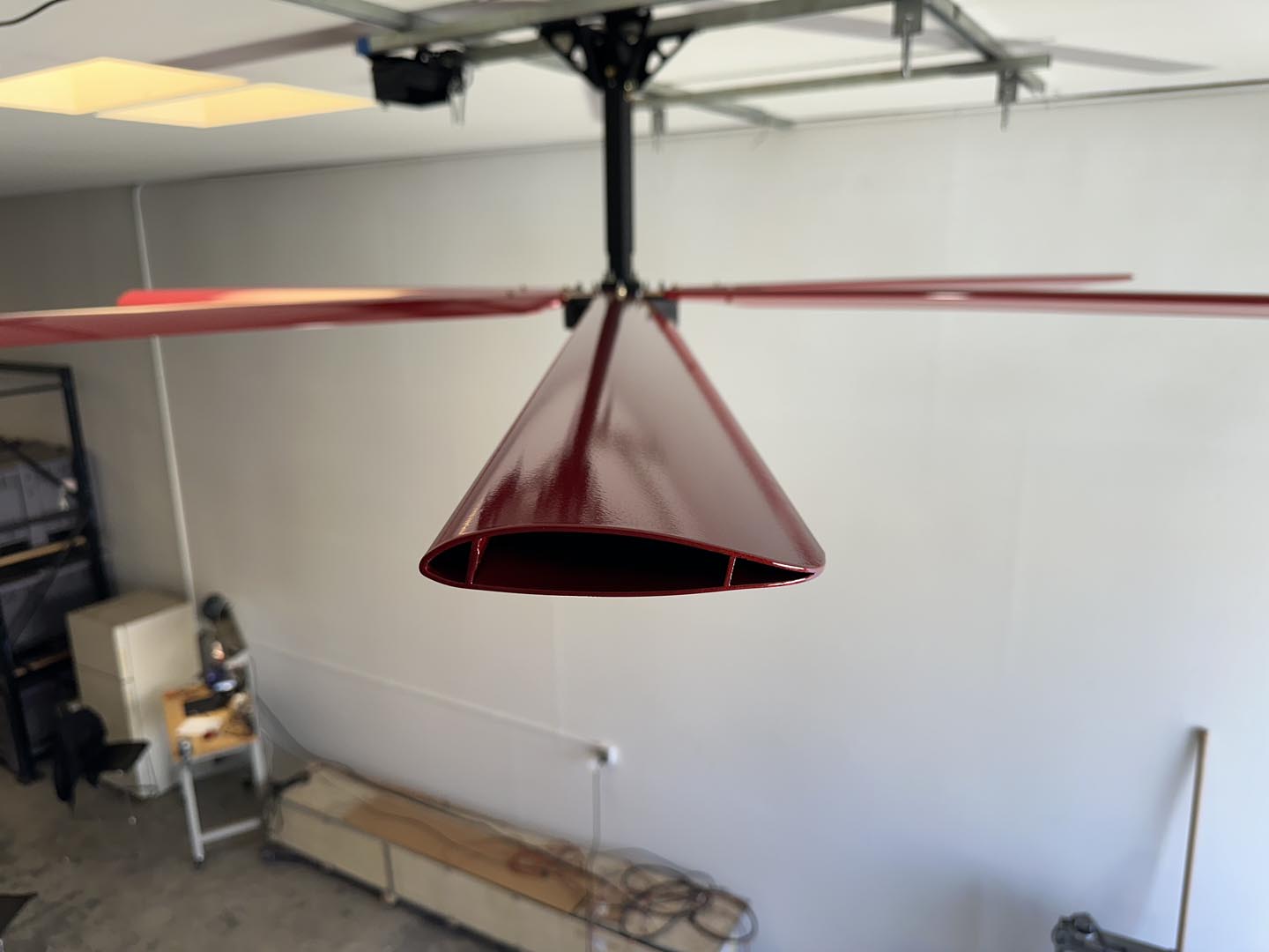 Close up of a telescoping mount, motor, and one of the blades for DF6 Red Industrial Ceiling Fan from Industrial Fan Co, mounted on the ceiling with a gray wall in the background