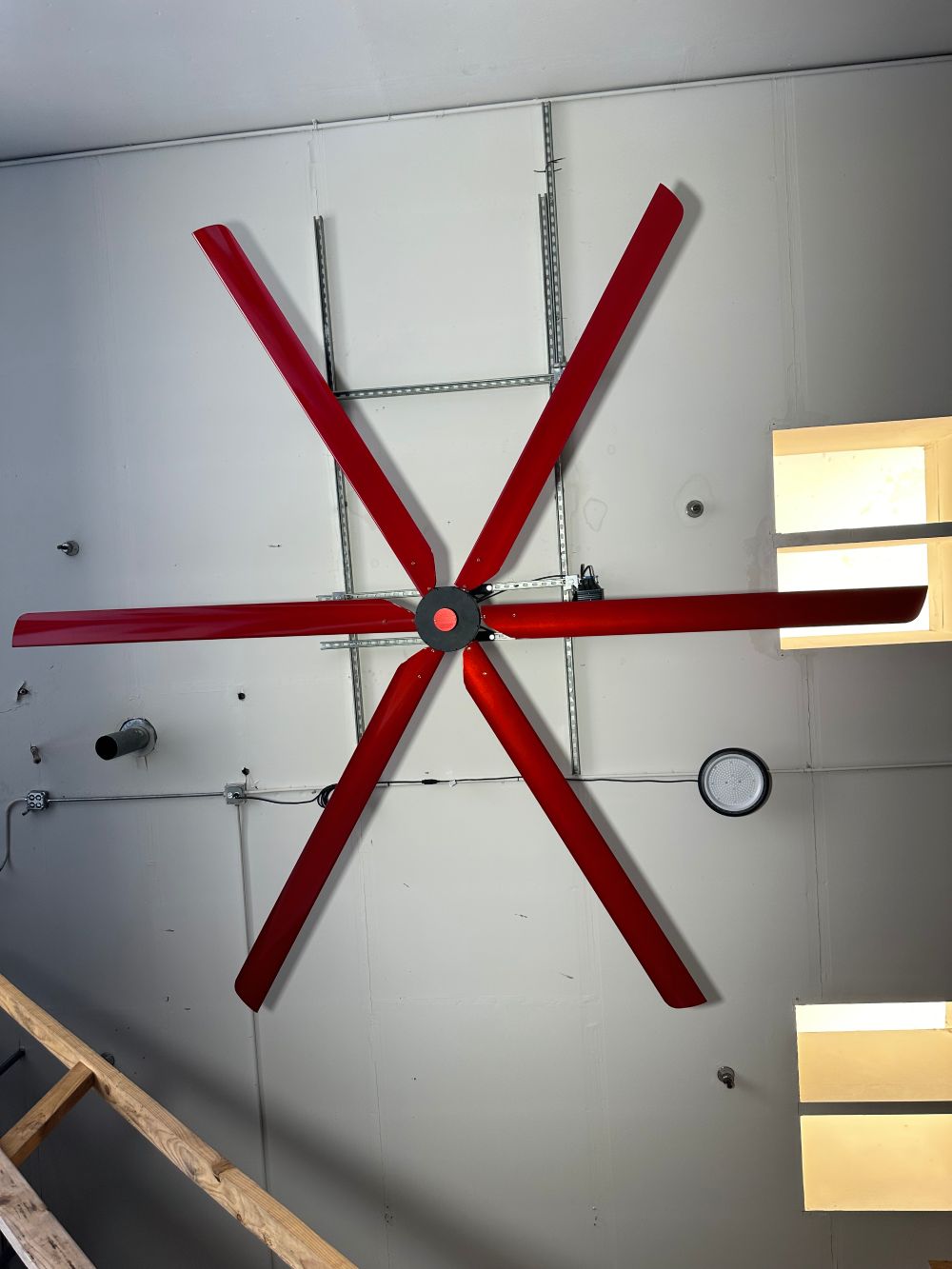 Full size picture of a wall mount, motor casing, red and silver brand badge and 6 blades for DF6 Red Industrial Ceiling Fan, product of Industrial Fan Co, mounted on the ceiling with yellow light fixtures around it