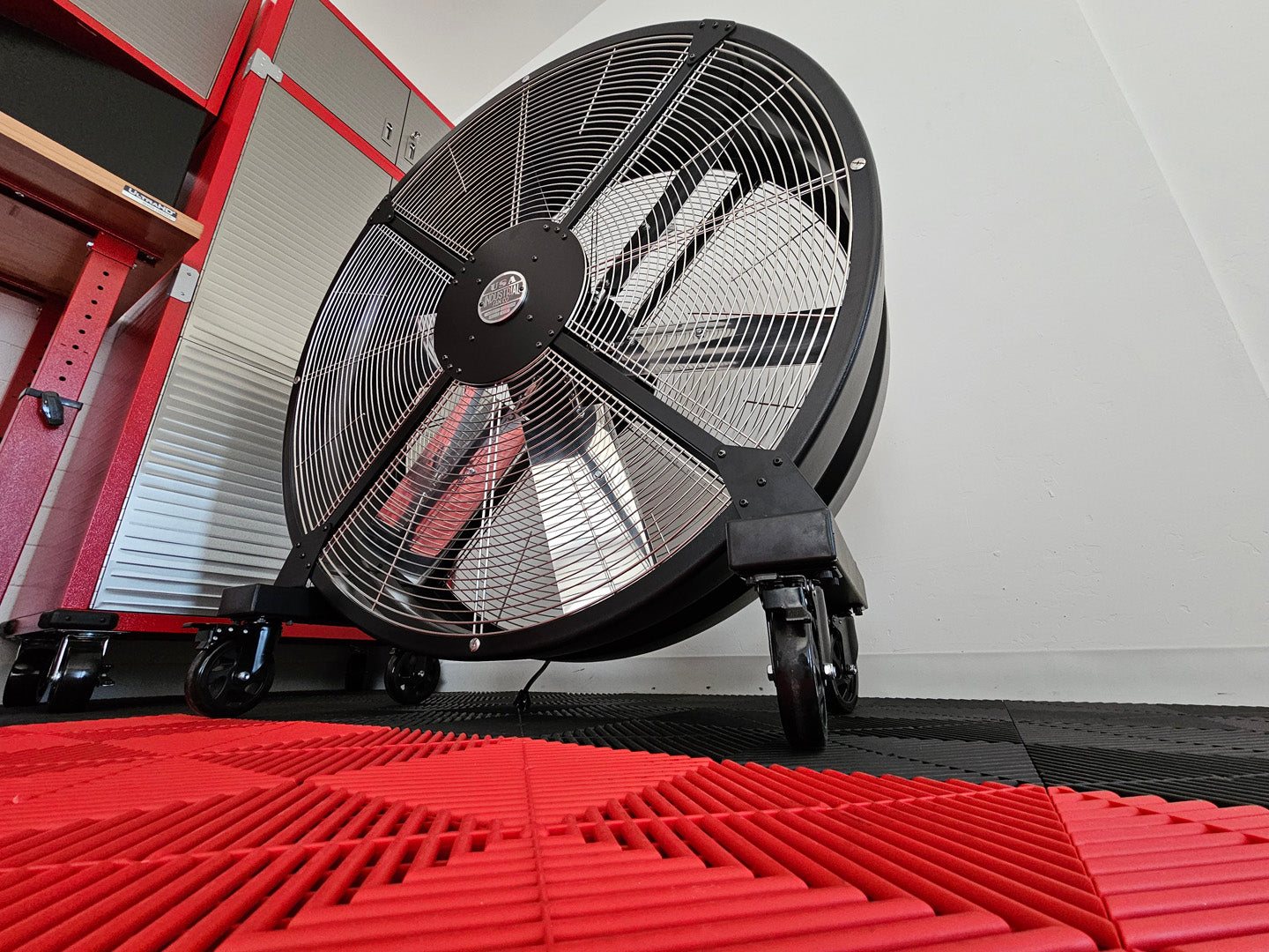 48" industrial floor fan on a red and black floor with a white wall background, with black housing, silver blades and silver brand badge, product of Industrial Fan Co