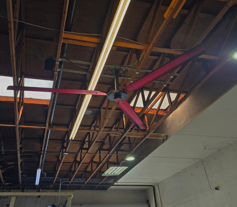 DF3 Red 3 blade Industrial Ceiling Fan, product of Industrial Fan Co, mounted on a wooden beam of a wooden roof, with a long light fixture behind it