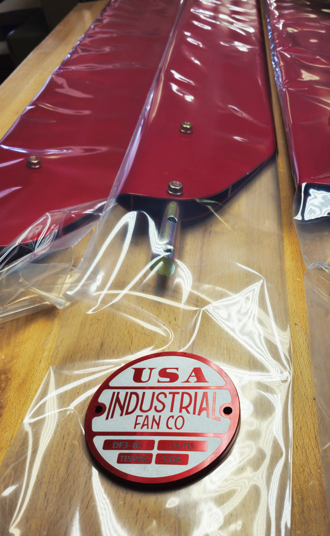Red and white Industrial Fan Co brand badge logo on a top of red fan blades covered with clear plastic bag with a blurred background.