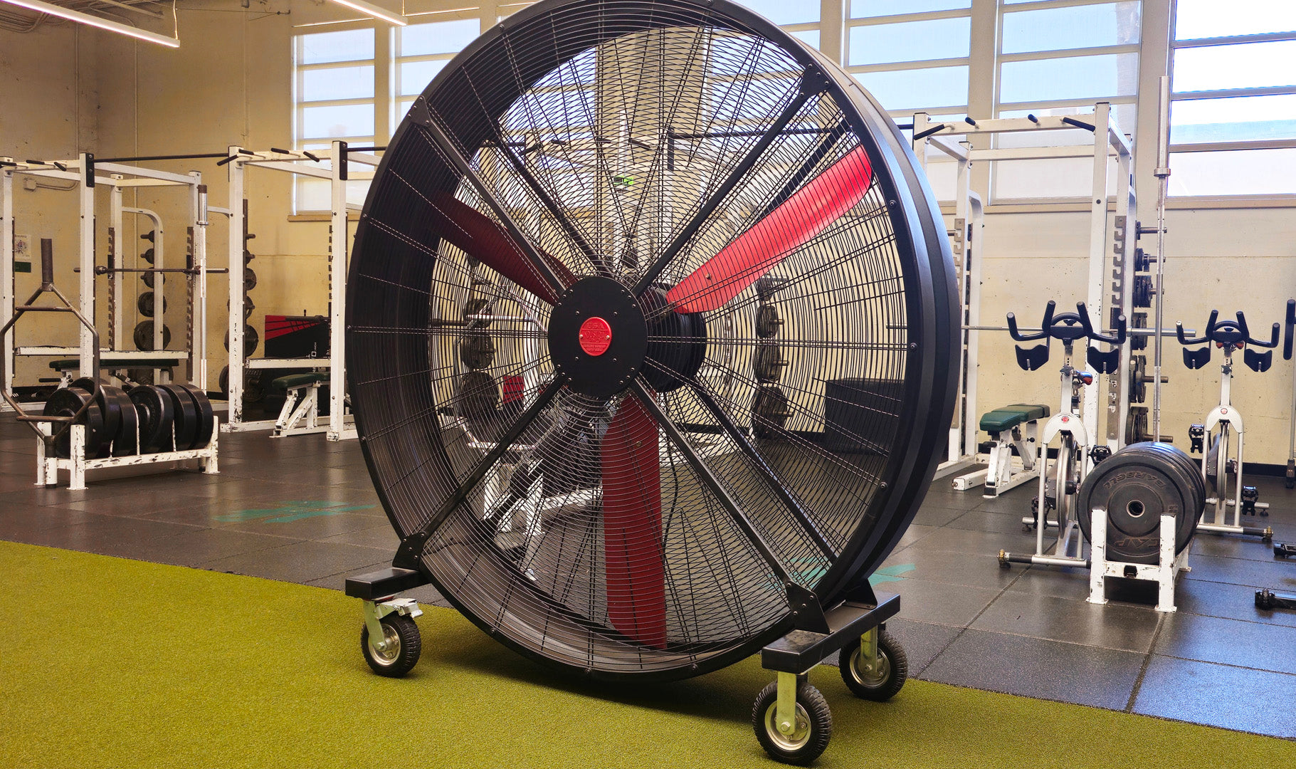 72" Floor Fan with black housing, red blades, metal frame, black and silver casters and metal bearings, product of Industrial Fan Co, in a high-school gym setting with workout equipment in the background