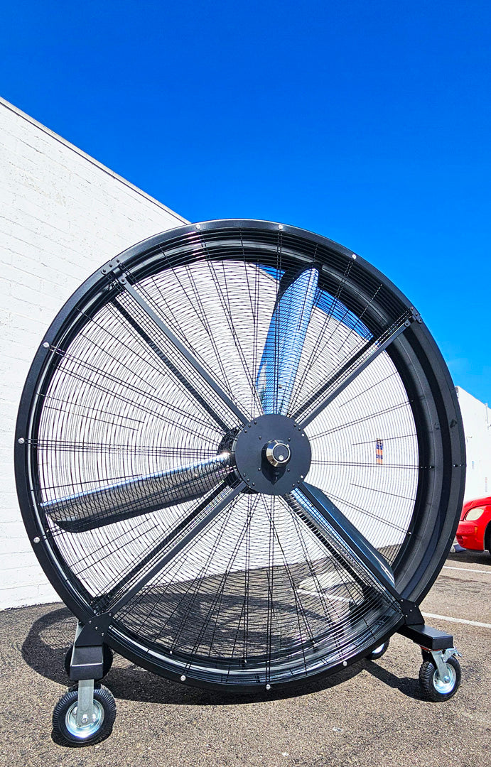 72" Floor Fan with black housing, polished aluminum silver blades, metal frame, black and silver casters, and metal bearings, product of Industrial Fan Co., in a parking lot