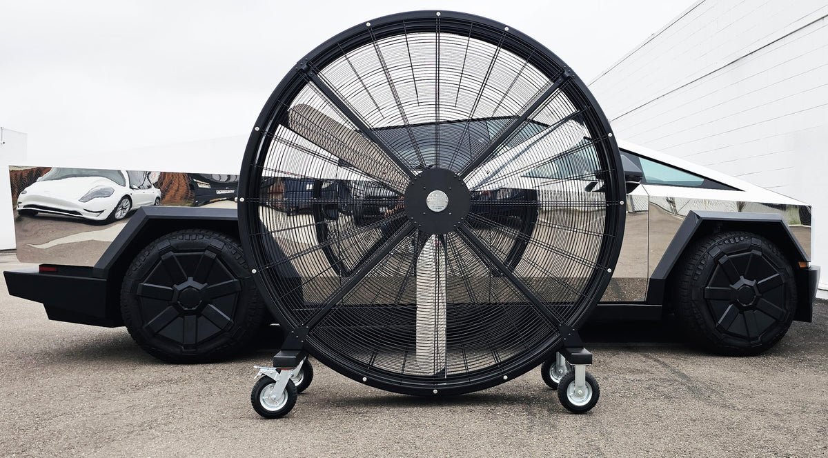 72" Floor Fan with black housing, polished aluminum silver blades, metal frame, black and silver casters and metal bearings, product of Industrial Fan Co, on a parking lot in front of a polished silver Tesla CyberTruckv