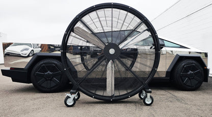 72" Floor Fan with black housing, polished aluminum silver blades, metal frame, black and silver casters and metal bearings, product of Industrial Fan Co, on a parking lot in front of a polished silver Tesla CyberTruckv