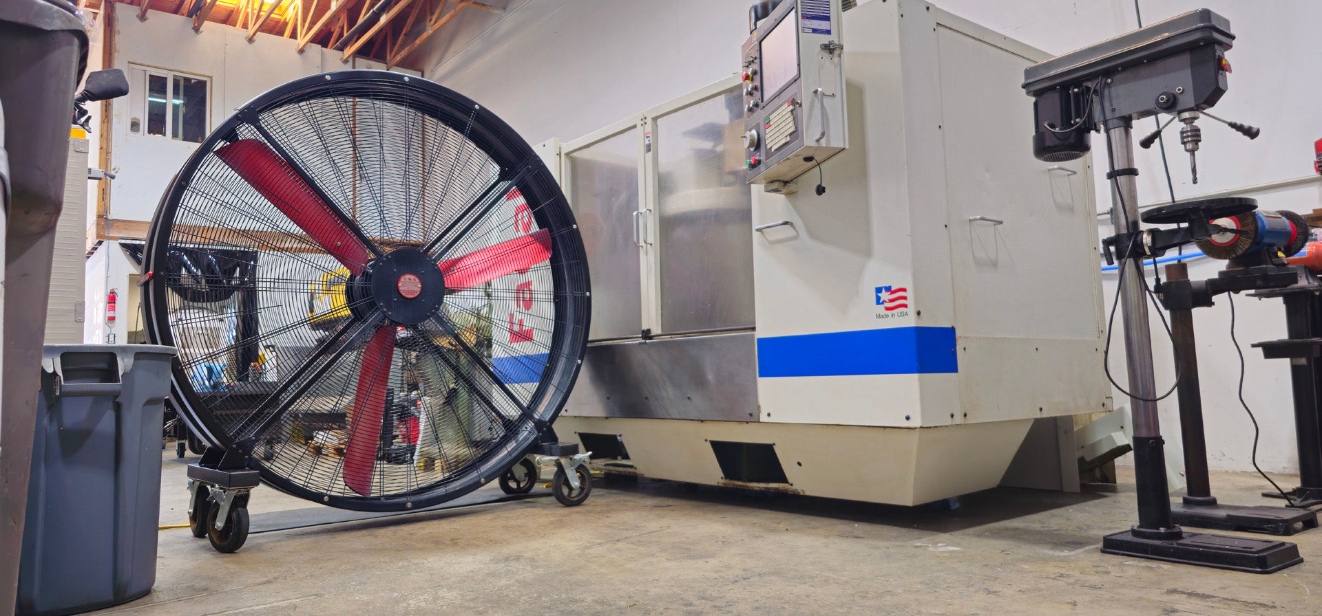 72" Floor Fan with black housing, red blades, metal frame, black and silver casters and metal bearings, product of Industrial Fan Co, in a industrial hangar setting surround by industrial machines
