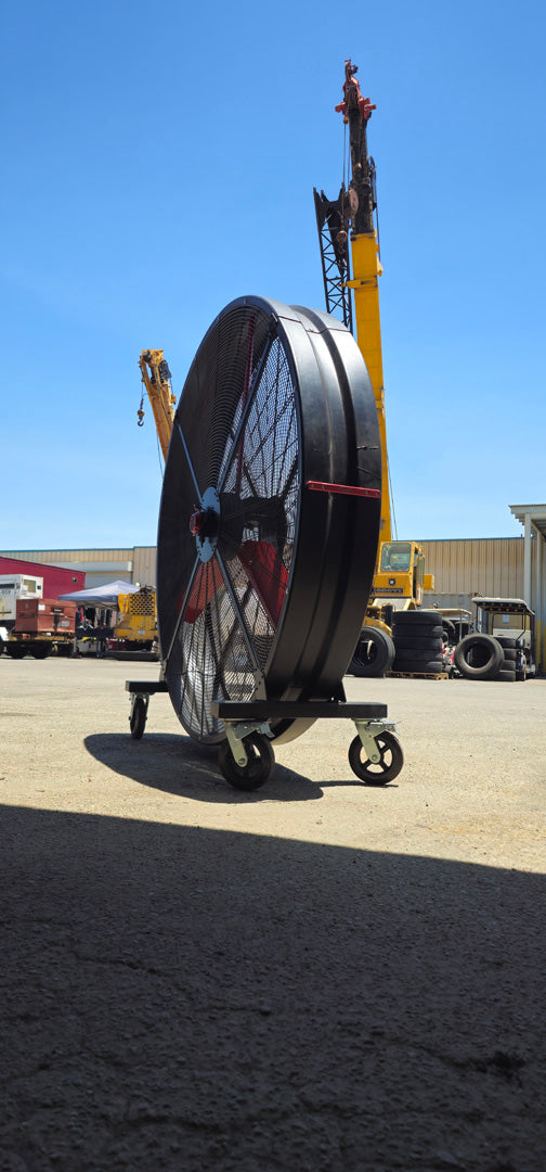 72" Floor Fan with black housing, red blades, metal frame, black and silver casters and metal bearings, product of Industrial Fan Co, in an industrial setup with cranes in the background