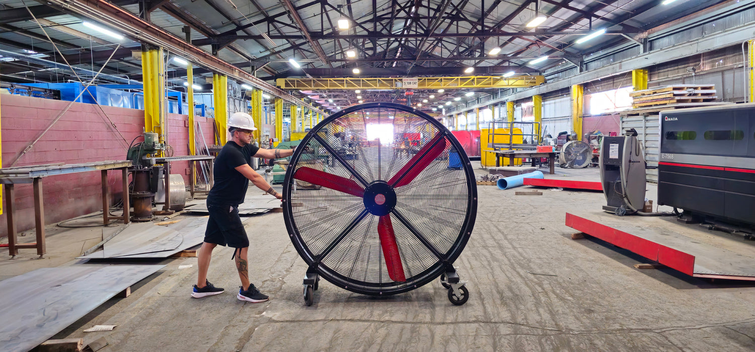 72" Floor Fan with black housing, red blades, metal frame, black and silver casters and metal bearings, product of Industrial Fan Co, in a large industrial hangar being pushed by a man 